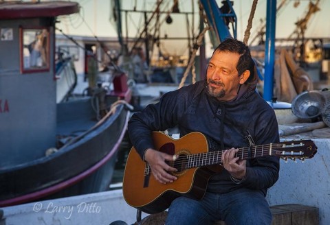 Strumming his guitar, this fisherman was relaxing at the end of the day as other fishing boats were still unloading oysters, Fulton Harbor, Fulton, Texas