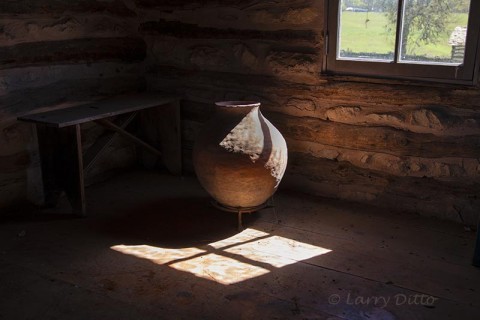 Clay jar by log cabin window.